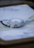 Close-up of a Cerakote Snow White Field-1 timer watch featuring a lumed ARES arrow crown on a Multicam Alpine white camouflage-patterned strap.