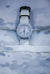 Close-up of a Cerakote Snow White Field-1 timer watch featuring a lumed ARES arrow crown on a Multicam Alpine white camouflage-patterned strap in a matching Alpine 4-slot ARES watch roll 